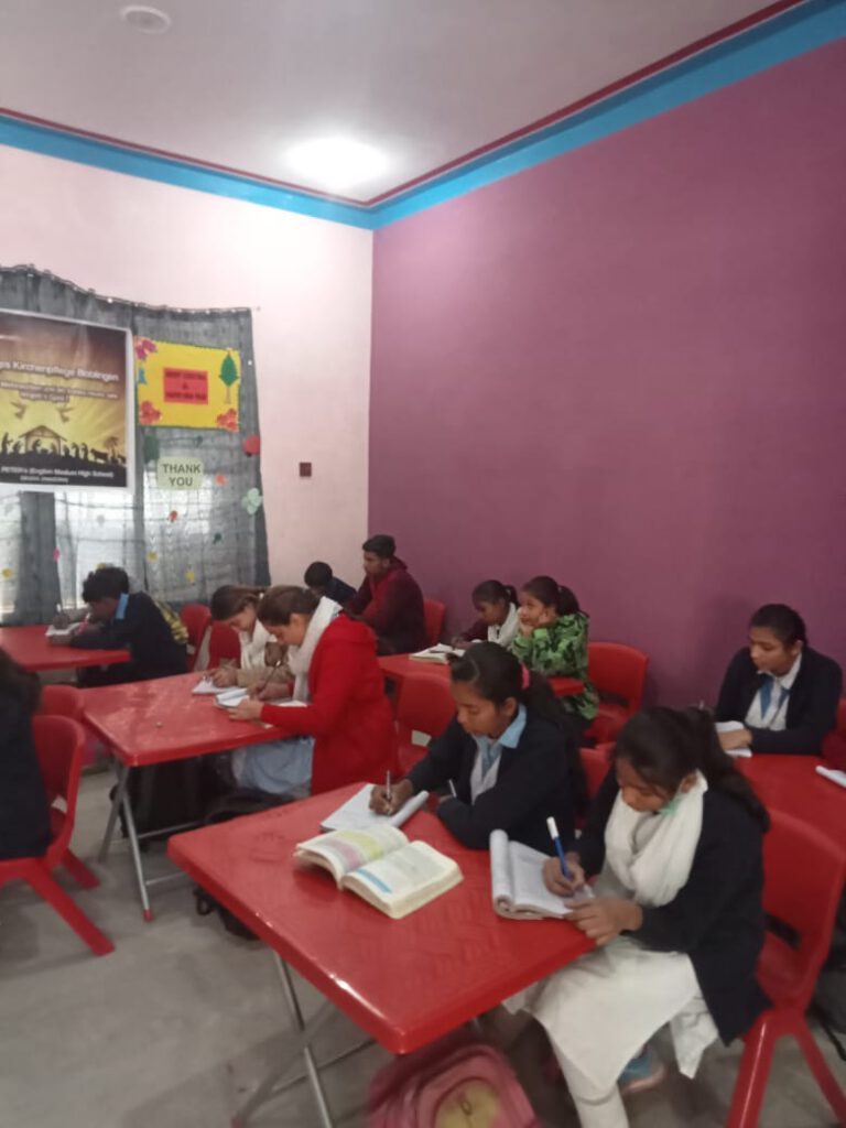 Klassenzimmer mit neuen knallroten Schulmöbeln und einer Gruppe von Schülerinnen und Schülern, die gerade Unterricht haben.