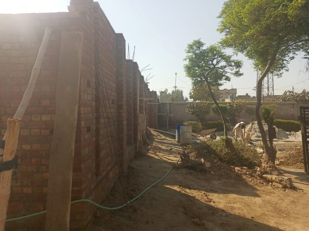 Picture showing the building with completed walls but without roof on the left and the yard before the building on the right.