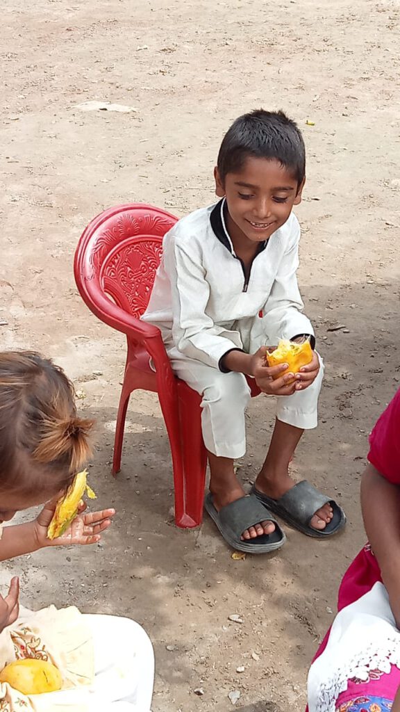 A young boy sitting in a chair and enjoying a mango fruit.