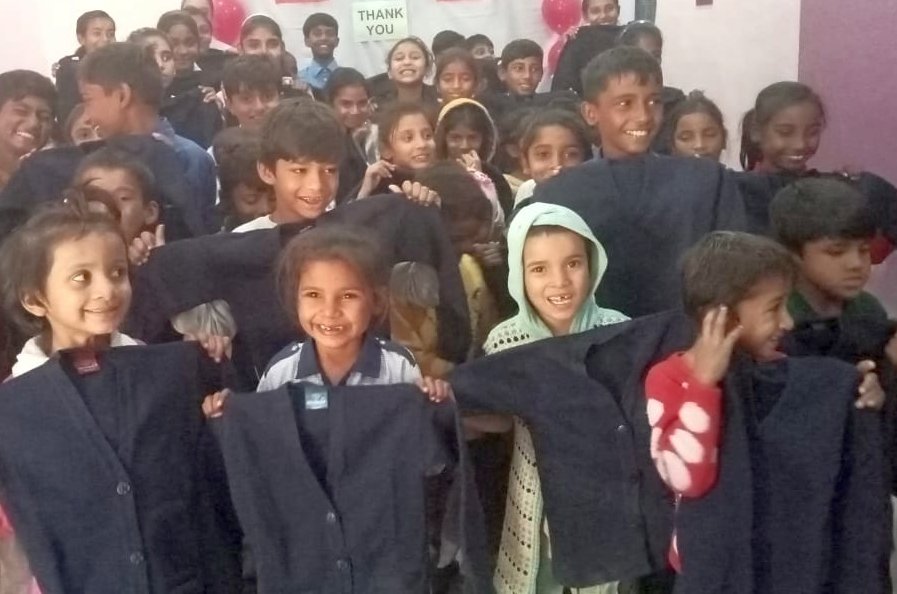 Many smiling students lifting up the new sweaters they received as gifts.