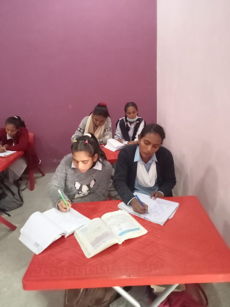 Classroom with new red furniture with several girls writing in their notebooks.